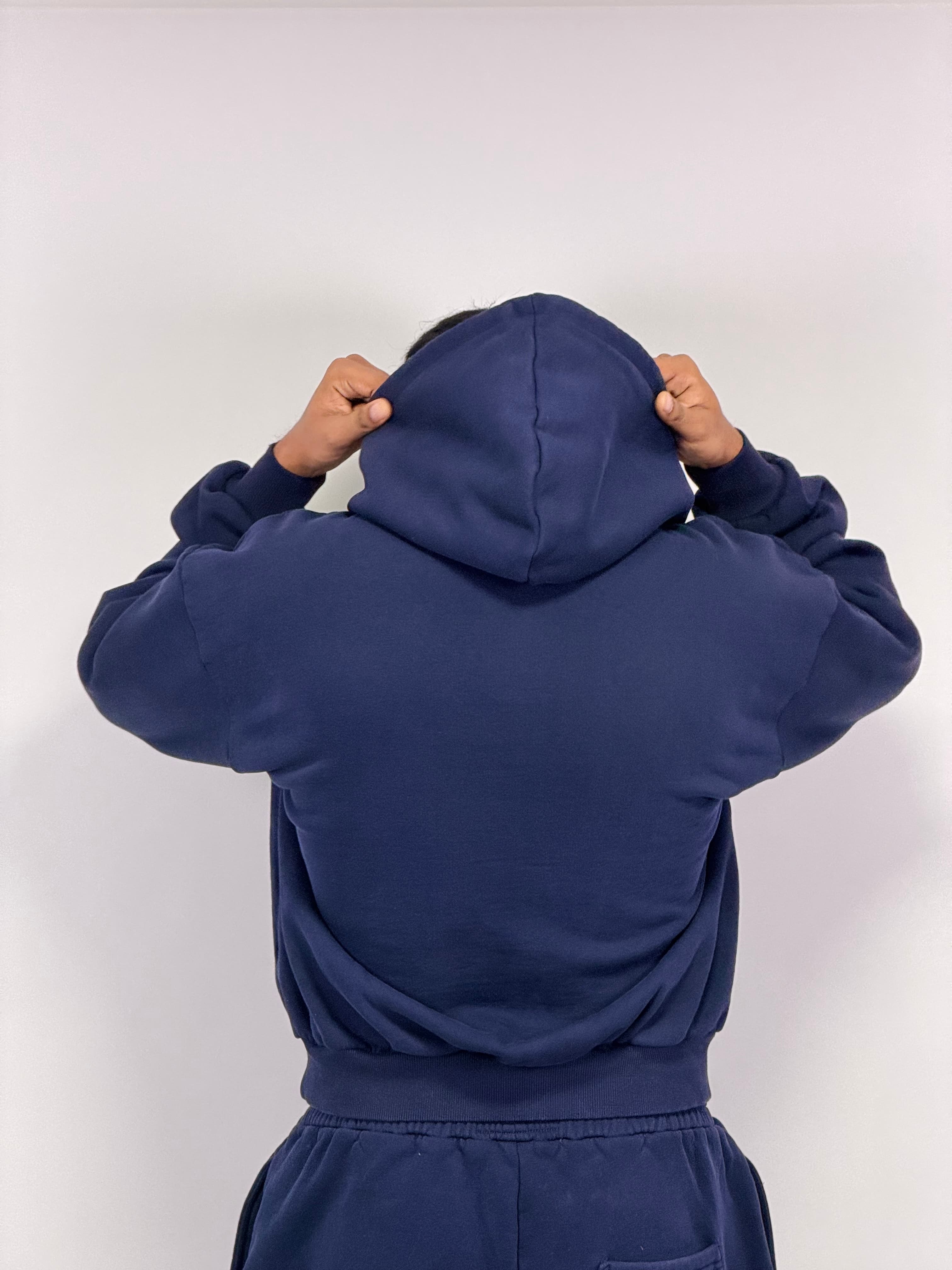Model pulling on the hood of a navy VadaWear hoodie, back view